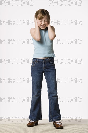 Smiling girl (8-9) covering her ears, studio shot. Photo : Rob Lewine