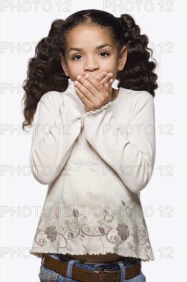 Studio portrait of girl (8-9) with pigtails covering mouth with hands. Photo : Rob Lewine