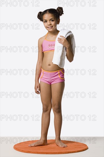 Studio portrait of girl (8-9) in bikini holding towel. Photo: Rob Lewine