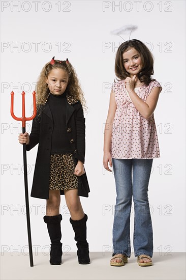 Studio portrait of two girls (8-9) wearing Halloween costumes with trident and halo. Photo: Rob Lewine