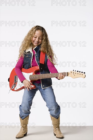 Studio portrait of smiling girl (8-9) playing electric guitar. Photo: Rob Lewine