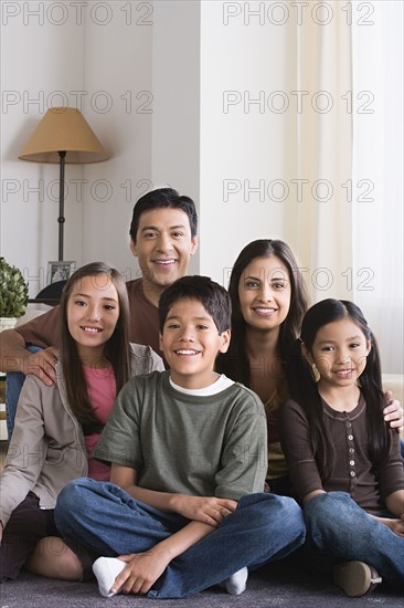 Portrait of happy family with three children (8-9, 10-11) sitting on floor. Photo : Rob Lewine