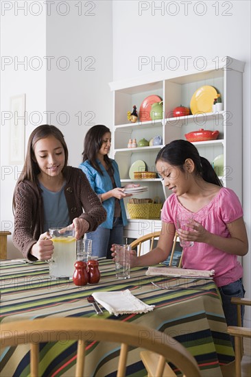 Mother with two daughters (8-9, 10-11) cleaning from table. Photo: Rob Lewine