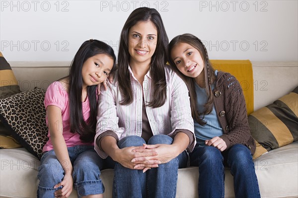Portrait of happy mother with two daughters (8-9, 10-11) sitting on sofa. Photo : Rob Lewine