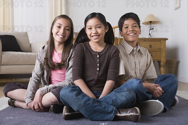 Portrait of happy children (8-9, 10-11) sitting on floor. Photo : Rob Lewine