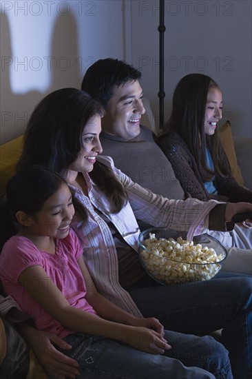 Family with two daughters (8-9, 10-11) watching tv on sofa. Photo : Rob Lewine