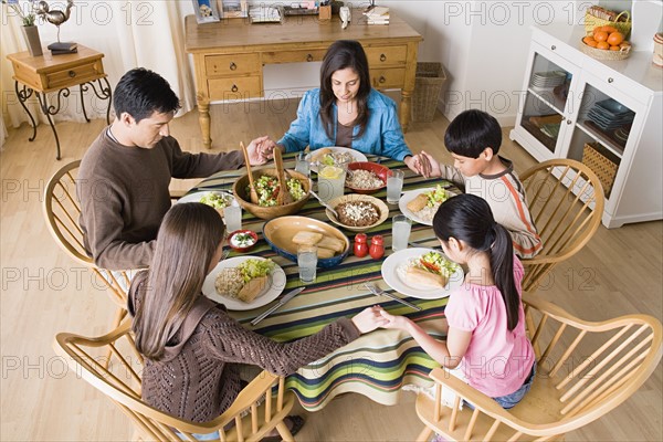 Family with three children (8-9, 10-11) praying at table before dining. Photo : Rob Lewine