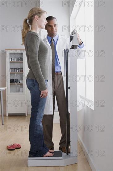 Male doctor measuring woman's weight. Photo : Rob Lewine