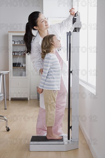 Female doctor measuring girl's (4-5) weight. Photo : Rob Lewine