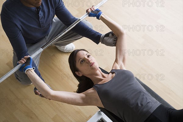 Woman lifting barbell while instructor assisting her. Photo : Rob Lewine