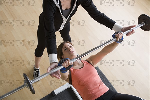 Woman lifting barbell while instructor assisting her. Photo: Rob Lewine