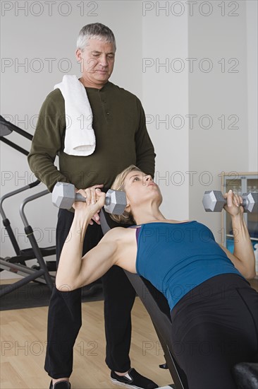 Woman lifting dumbbells while instructor assisting her. Photo : Rob Lewine