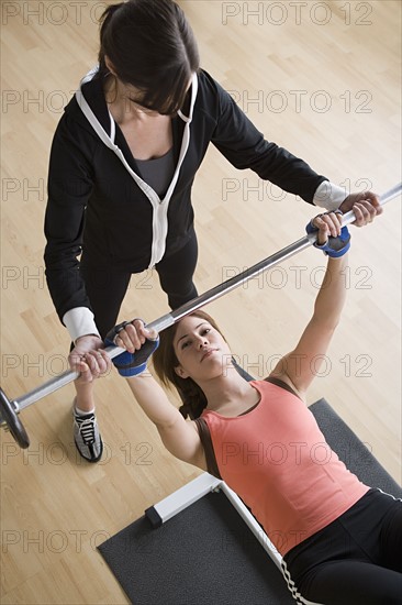 Woman lifting barbell while instructor assisting her. Photo: Rob Lewine