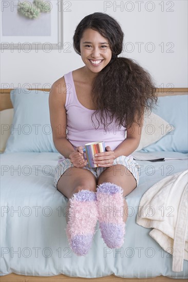 Young woman sitting on bed. Photo : Rob Lewine