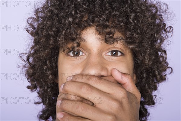 Portrait of teenage boy (14-15) covering mouth with hands. Photo : Rob Lewine