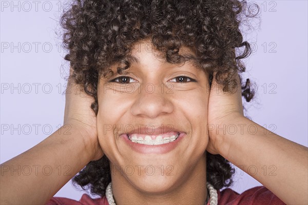Portrait of teenage boy (14-15) covering ears with hands. Photo : Rob Lewine