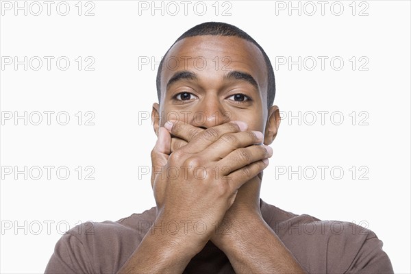 Studio portrait of young man with hands on his mouth. Photo: Rob Lewine