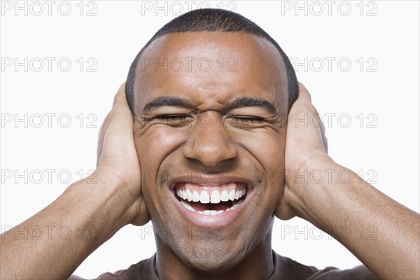 Studio portrait of young man with hands on his ears. Photo : Rob Lewine