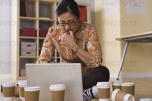 Woman working on laptop surrounded by empty coffee cups. Photo: Rob Lewine