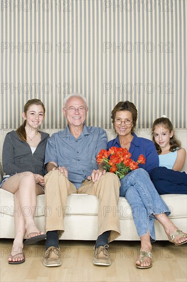 Portrait of grandparents with two granddaughters (8-9, 14-15) sitting together on sofa. Photo : Rob Lewine