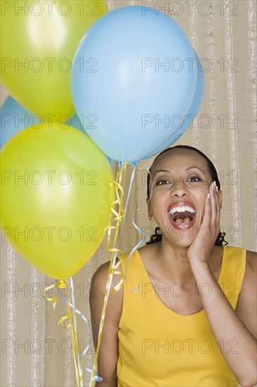 Happy mid adult african woman shouting while holding yellow and blue balloons. Photo : Rob Lewine