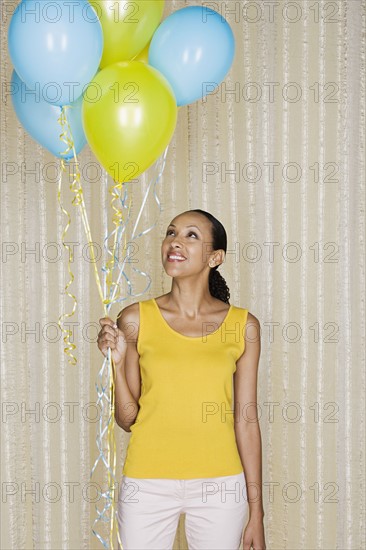 Portrait mid adult african woman holding yellow and blue balloons. Photo: Rob Lewine