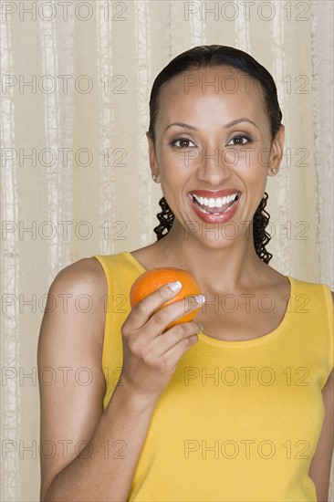 Portrait of smiling woman holding orange, studio shot. Photo : Rob Lewine