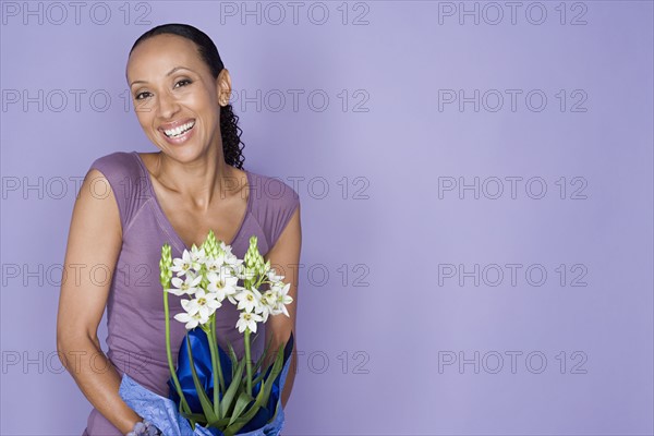 Portrait of smiling woman holding flowers on purple background, studio shot. Photo : Rob Lewine