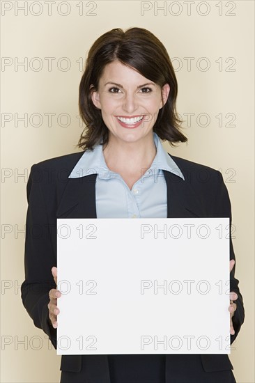 Portrait of smiling businesswoman holding blank page, studio shot. Photo : Rob Lewine