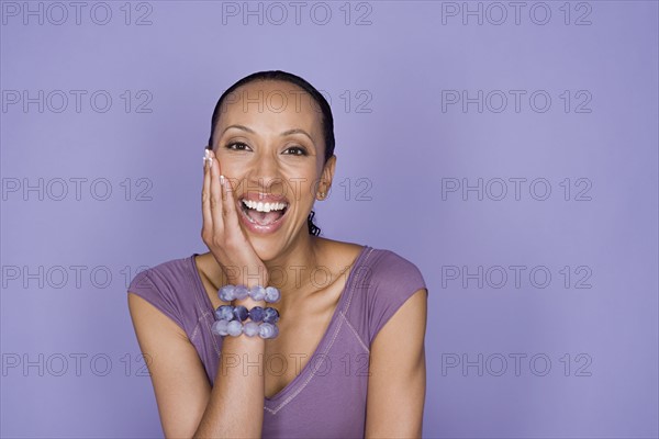 Portrait of smiling woman sitting on purple background, studio shot. Photo : Rob Lewine