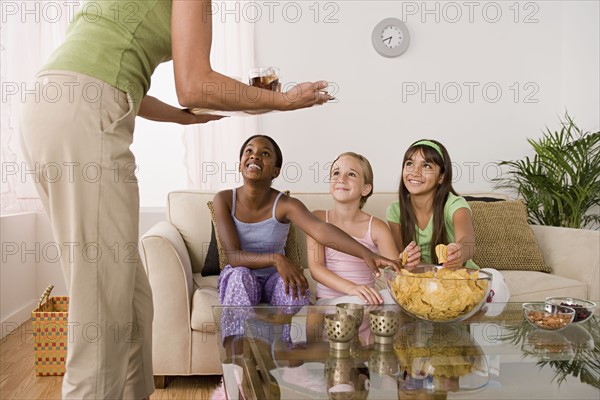 Woman serving food for three girls (10-11) at slumber party. Photo: Rob Lewine