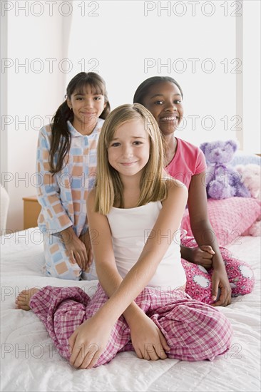 Portrait of three girls (10-11) sitting on bed at slumber party. Photo: Rob Lewine