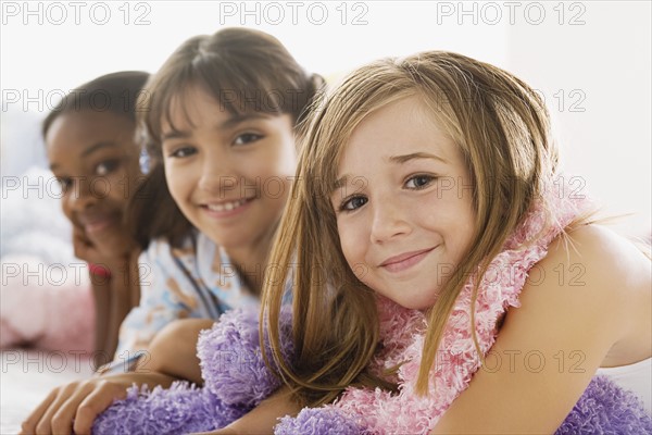 Portrait of three girls (10-11) lying on bed at slumber party. Photo: Rob Lewine