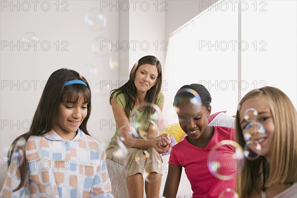 Three girls (10-11) and woman blowing bubbles at slumber party. Photo : Rob Lewine