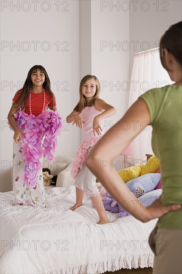 Two girls (10-11) jumping on bed at slumber party while woman watching them. Photo : Rob Lewine