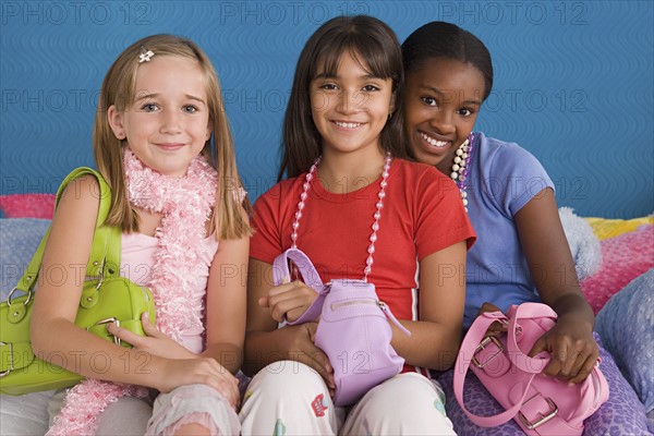 Portrait of three girls (10-11) with purses on sofa. Photo: Rob Lewine