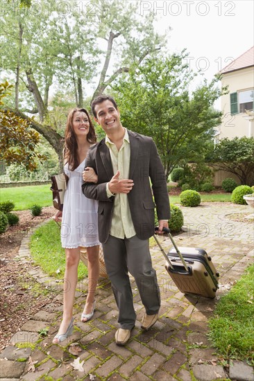 USA, New Jersey, Smiling couple with suitcase walking on footpath. Photo: Tetra Images