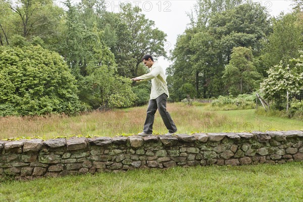 USA, New Jersey, Man walking on stone wall on field. Photo : Tetra Images