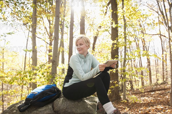 Female hiker using digital tablet in forest. Photo : Tetra Images