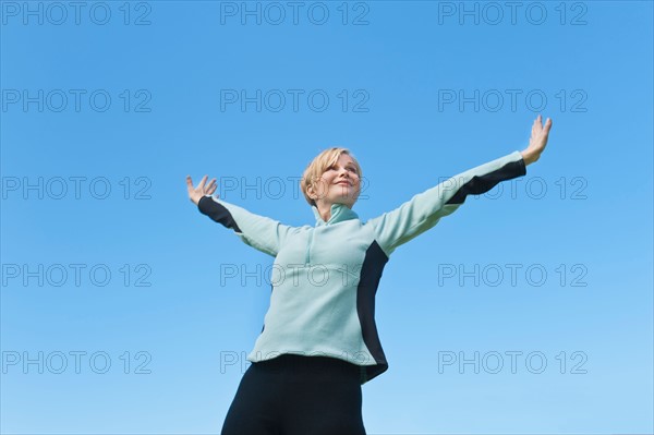 Woman with arms raised against blue sky. Photo: Tetra Images