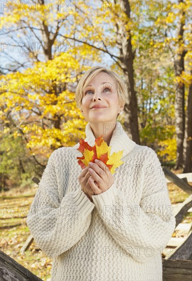 Smiling woman holding leaves in Autumn forest. Photo : Tetra Images