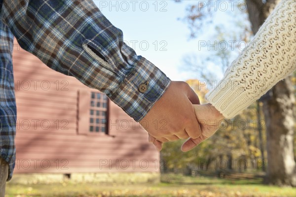 Close-up of couple holding hands in front of cottage house. Photo : Tetra Images