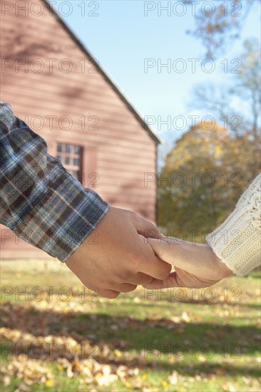 Close-up of couple holding hands in front of cottage house. Photo : Tetra Images