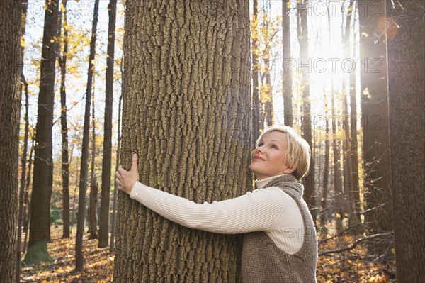 USA, New Jersey, Smiling woman hugging tree in Autumn forest. Photo: Tetra Images