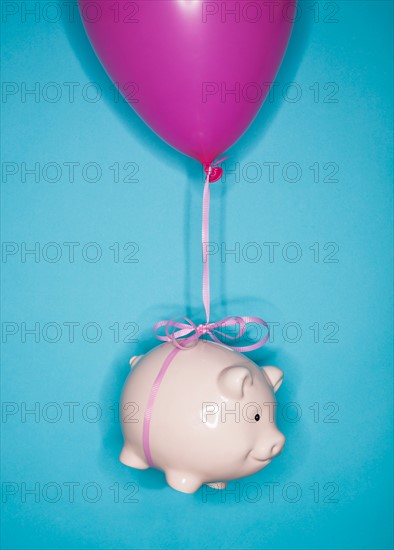 Studio shot of piggy bank lifted by balloon.
