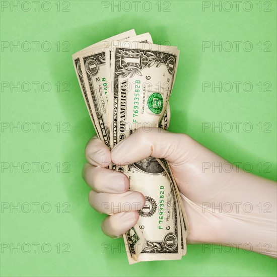 Hand in surgical glove holding banknotes.