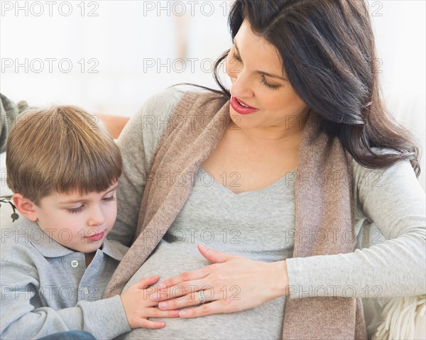 Boy (4-5) touching pregnant mother's belly.