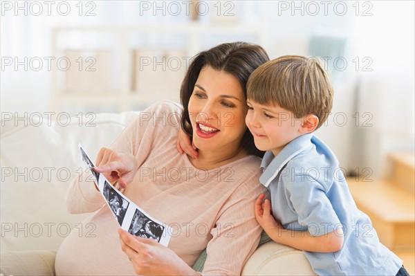 Pregnant woman with son (4-5) looking at ultrasound photo.