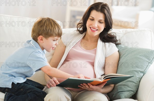 Mother and son (4-5) reading book on sofa.