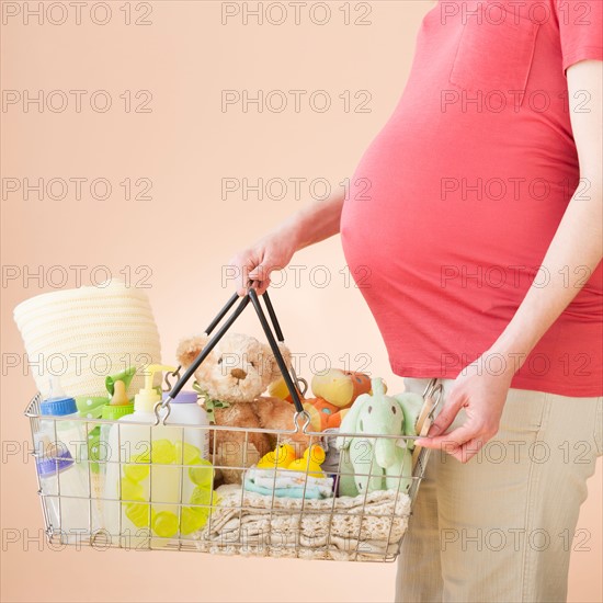 Studio shot of woman with shopping basket full of baby goods, midsection.